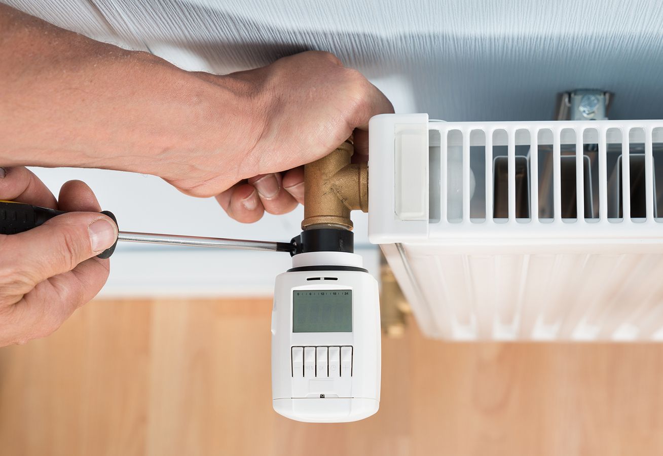 Installateur montiert Thermostat an Heizkörper